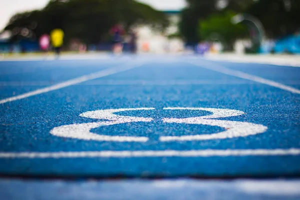 Koşu yolunun başlangıcında sekiz numara. Farklı numaralar ve beyaz çizgilerle mavi koşu bandı. Seçmeli olarak Numara 'ya odaklan. Arkaplan mavisi. Kapat.