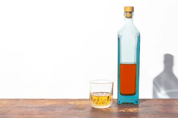 Beyaz arka plandaki eski ahşap masada bir şişe ve bir bardak alkol.