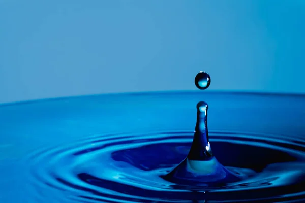 Water Druppel Plons Een Glazen Beker Blauw Gekleurd — Stockfoto