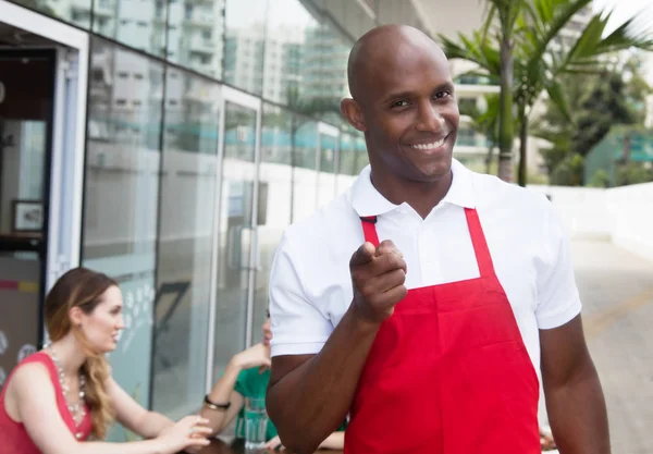African waiter at work in a restaurant pointing at camera