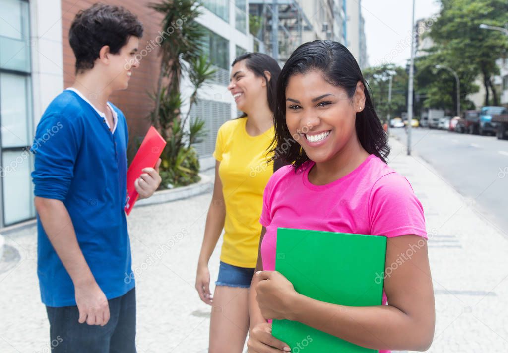 Happy latin female student in pink shirt with other students
