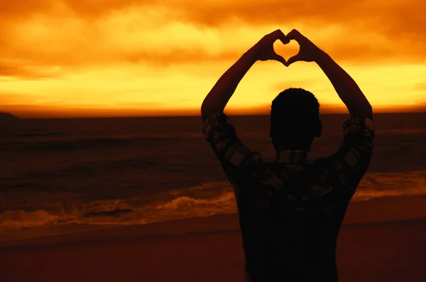 Mens in liefde vormen hart op strand bij zonsondergang — Stockfoto