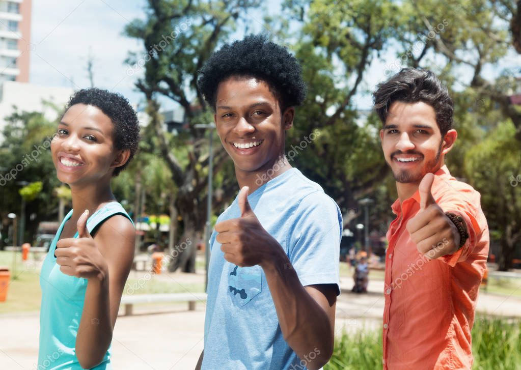 Group of three latin american young adults showing thumbs in cit