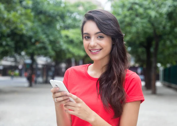 Rindo menina com camisa vermelha navegar na rede com telefone — Fotografia de Stock