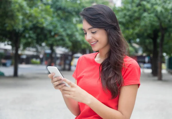 Όμορφο κορίτσι με το κόκκινο πουκάμισο σερφάροντας στο διαδίκτυο με το τηλέφωνό — Φωτογραφία Αρχείου