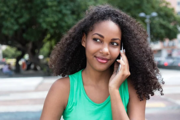 Sorrindo mulher latina com cabelo encaracolado e camisa verde no telefone em — Fotografia de Stock