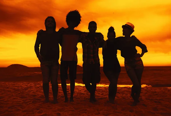 Grupo de hombres y mujeres brazo en brazo en la playa al atardecer —  Fotos de Stock