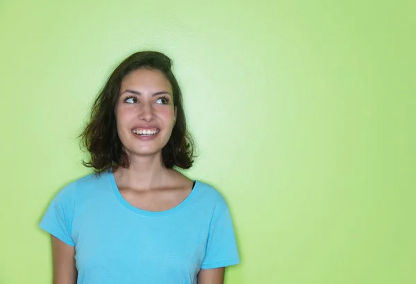 Mulher caucasiana jovem olhando para os lados de uma parede verde — Fotografia de Stock