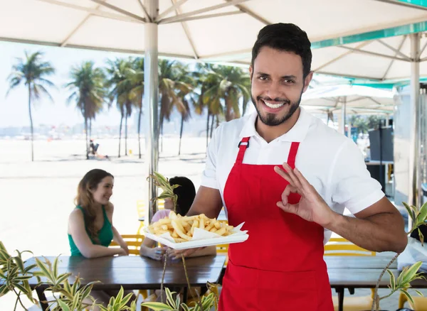 Щасливий офіціант, який подає картоплю фрі на пляжному барі — стокове фото