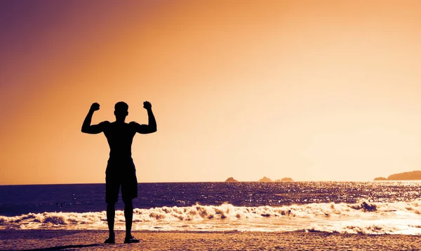 Hombre fuerte animando en la playa al atardecer — Foto de Stock