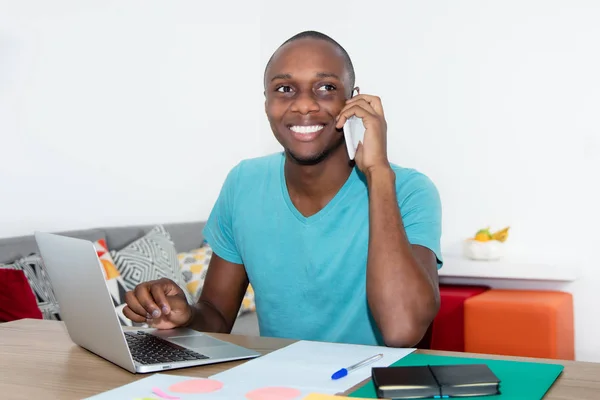 Skrattande afroamerikanska mannen skicka meddelande med telefonen hemma — Stockfoto