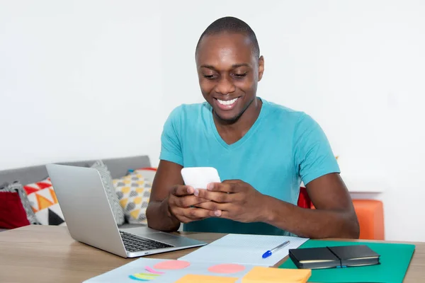 Skrattande afroamerikanska mannen skicka meddelande med telefonen hemma — Stockfoto