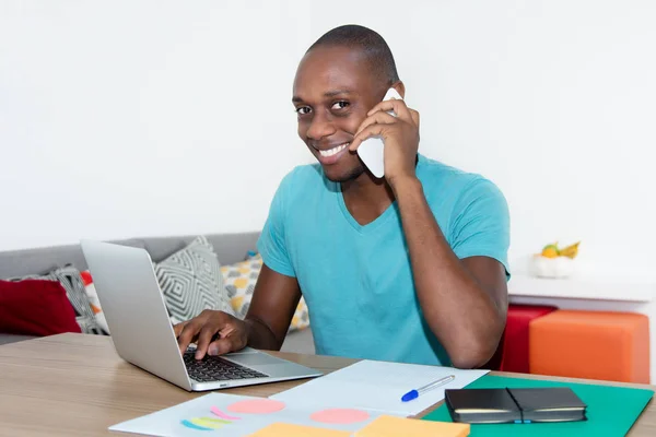 Homem afro-americano rindo trabalhando com computador e falando — Fotografia de Stock