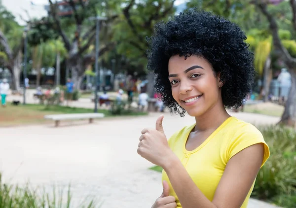 Fiatal felnőtt nő nevetve mutatja a hüvelykujj u göndör fekete hajjal — Stock Fotó