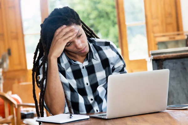 Tänkande latinamerikanska man med dreadlocks på dator — Stockfoto