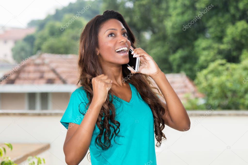 Cheering african american woman with long hair at mobile phone