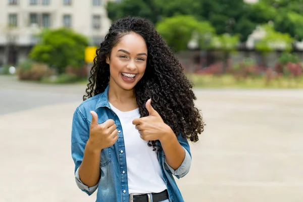 Braziliaans meisje met krullend haar en beugels tonen beide duimen omhoog — Stockfoto