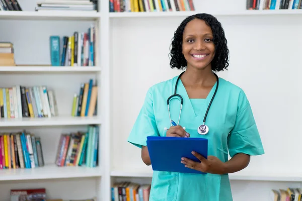 Laughing african american mature nurse with clipboard — Stock Photo, Image