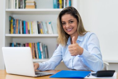 Bilgisayarın başparmağını gösteren sarışın olgun bir iş kadını.