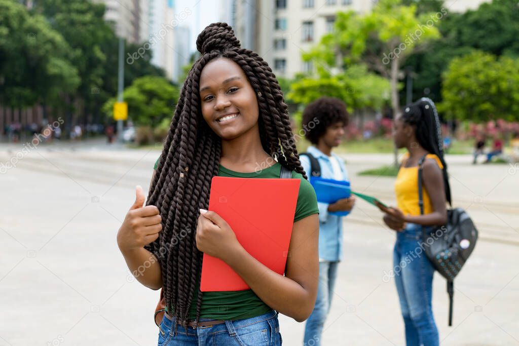 Laughing african american female student with amazing hairstyle outdoor in summer in city