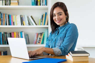 Üniversitede bilgisayar başında çalışan gülen genç bir kız öğrenci.