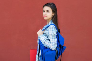 Sırt çantasıyla kameraya bakan beyaz kız öğrencinin portresi.