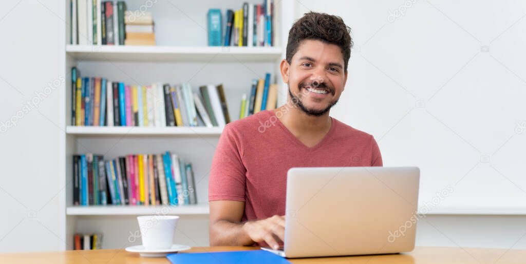 Laughing latin american man with beard working at computer at home