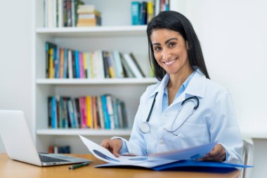 Hastanede çalışan Latin Amerikalı kadın doktor gülüyor.
