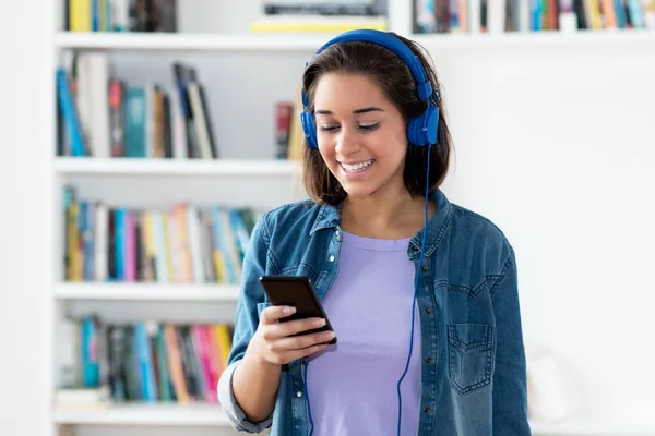 Spanish young adult woman listening to podcast indoors at home