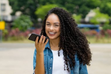Brezilya 'lı genç bir kadın yazın şehir dışında akıllı telefon ses tanıma sistemi kullanıyor.