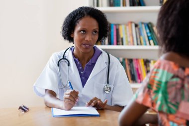 Olgun Afro-Amerikan kadın doktor hastanedeki hastaya koronavirüs semptomlarını açıklıyor.