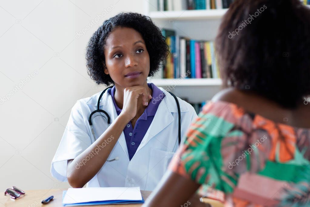 Mature african american female doctor listening to patient with pain and coronavirus symptoms at hospital