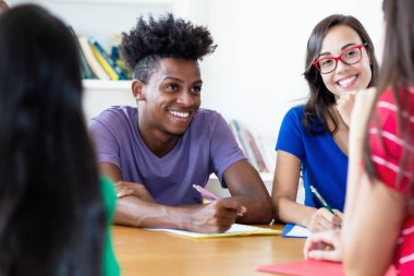 Üniversitenin sınıfında bir grup etnik çeşitliliğe sahip öğrenciyle birlikte gülen Afrikalı Amerikalı erkek öğrenci.