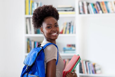 Üniversite sınıfında sırt çantası ve evrak işleriyle gülen Afro-Amerikan bayan öğrenci.