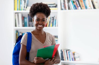 Üniversite sınıfında sırt çantası ve evrak işleriyle uğraşan Afro Amerikalı güzel bir bayan öğrenci.