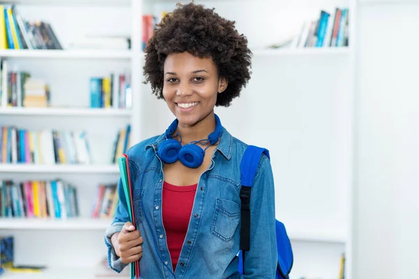 Sırt çantası ve evrak işleriyle üniversitenin çalışma odasında gülen Afrikalı Amerikalı kız öğrenci.