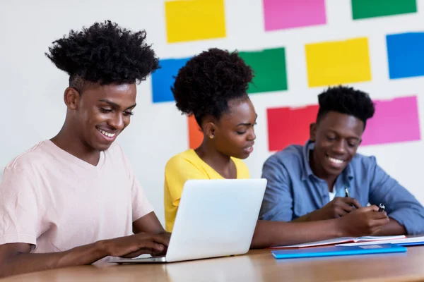 Laughing african american male student at computer with group of students at classroom of university or college