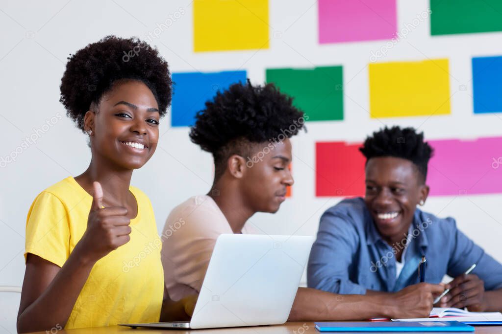 Pretty african american female student at computer with group of students at classroom of university or college
