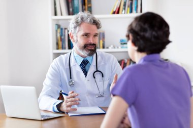 Hastane ya da klinikteki hastaya koronavirüs semptomlarını açıklayan olgun bir doktor.