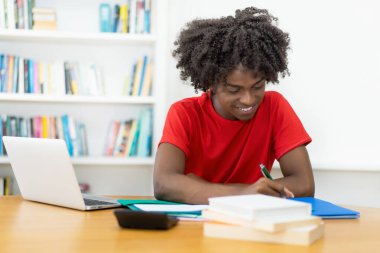 Afro-Amerikalı erkek öğrenci evde masa başında öğreniyor.