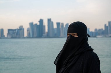 Doha şehrinin silueti yakınında niqab 'ı olan Müslüman bir kadın.