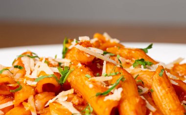 Penne Tüm Arrabbiata sosisleri, pastırma ve peynirli beyaz tabakta, ahşap masada fotokopi alanı ile..