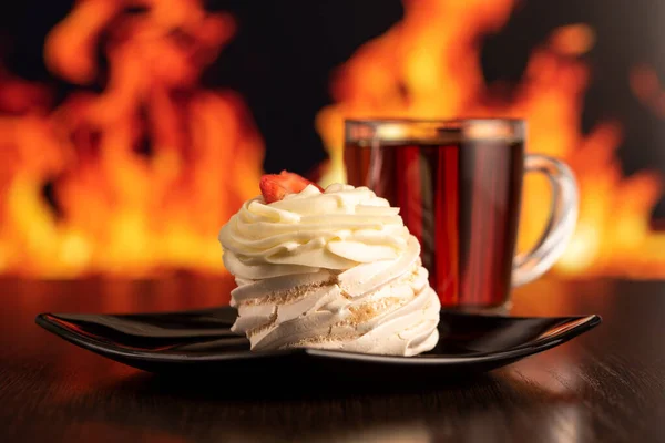 strawberry cake and hot tea on a wooden table with a blurry fire in the background. horizontal photo without people.