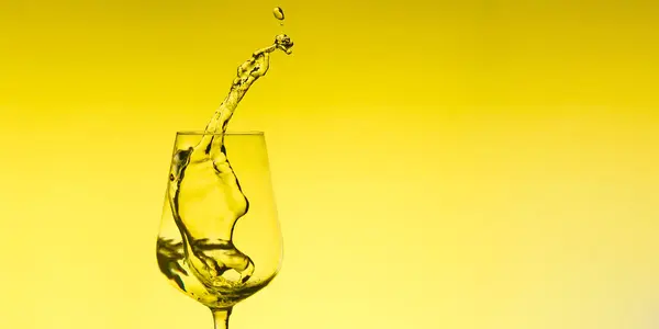 Bellissimi spruzzi d'acqua in un bicchiere di vino, con filtro giallo, da vicino con spazio per copiare . Foto Stock