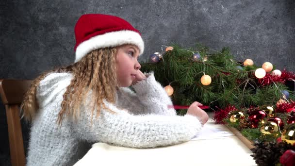 Kleines Mädchen schreibt einen Brief an den Weihnachtsmann. Emotionen: Freude, Glück, Nachdenklichkeit, Ermüdung... Weihnachten sollte schnell sein, damit der Weihnachtsmann Träume wahr werden lässt — Stockvideo