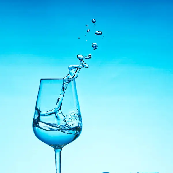Hermosas salpicaduras de agua en una copa de vino, con filtro azul, cerca con espacio de copia . — Foto de Stock