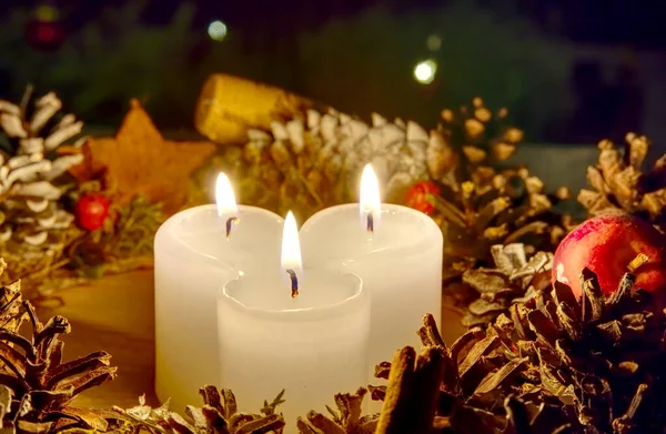 Drei brennende Kerzen mit Weihnachtsschmuck aus Tannenzapfen ringsum — Stockfoto