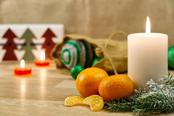 Burning candles, christmas decorations and mandarin. Green balls for Christmas tree and fir twig on wooden floor with bokeh background. Copy space — Stock Photo, Image