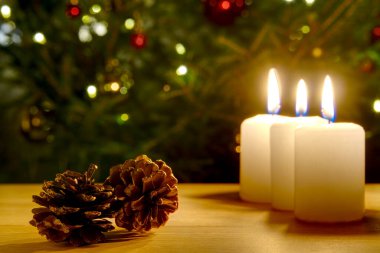 Etrafında çam kozalaklarının Noel süslemesiyle yanan üç mum.