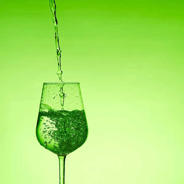 Hermosas salpicaduras de agua en una copa de vino, con filtro verde, cerca con espacio de copia . — Foto de Stock